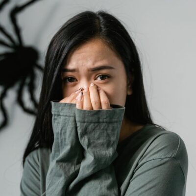 An anxious woman indoors with a large wall spider, depicting arachnophobia.