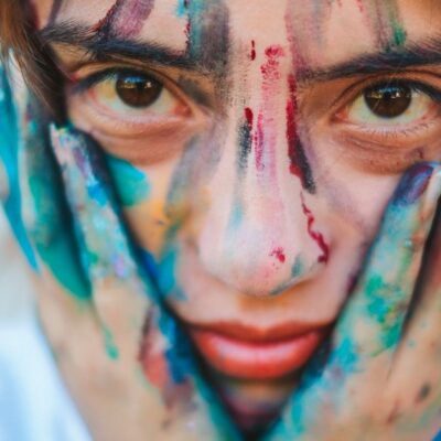 Close-up portrait of a young girl with a painted face and hands, showcasing creativity.