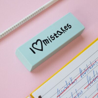 A blue eraser with 'I Love Mistakes' next to a pencil and crossed-out text on a pink background.