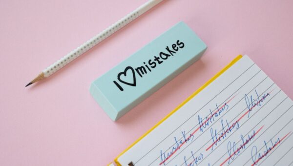 A blue eraser with 'I Love Mistakes' next to a pencil and crossed-out text on a pink background.