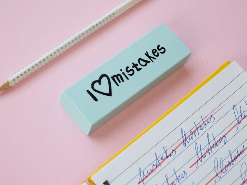 A blue eraser with 'I Love Mistakes' next to a pencil and crossed-out text on a pink background.