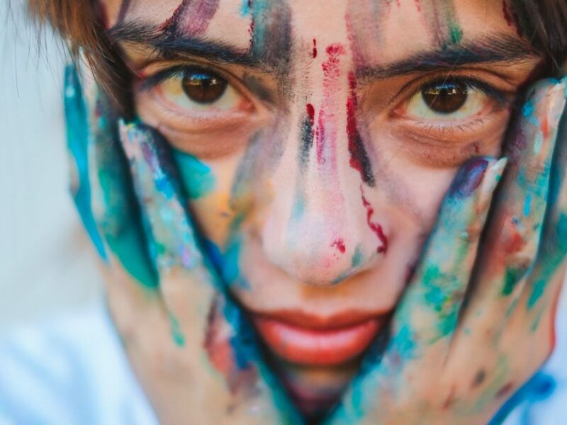 Close-up portrait of a young girl with a painted face and hands, showcasing creativity.