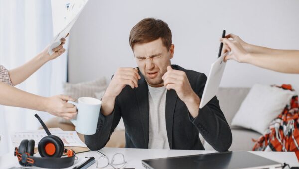 Adult man stressing out at home office desk with multiple demands surrounding him.