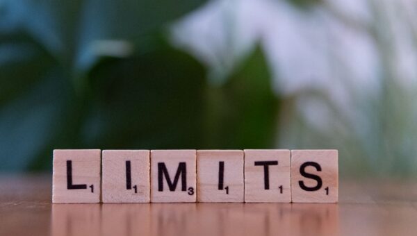 Wooden letter tiles forming the word 'LIMITS' on a wooden table.