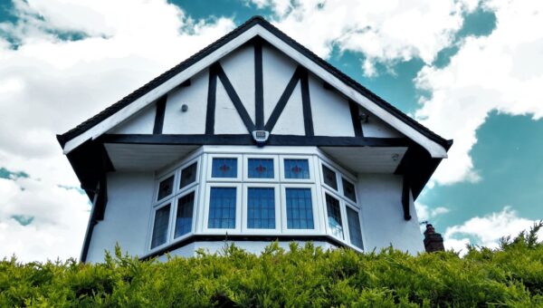 Tudor-style house facade with a bay window against a vibrant sky and greenery.