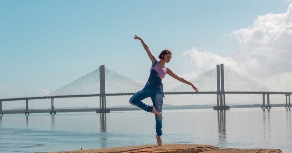 A woman performs a yoga pose on rocks near a scenic bridge over calm waters.