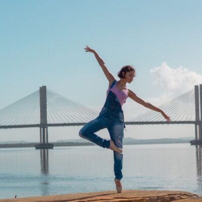 A woman performs a yoga pose on rocks near a scenic bridge over calm waters.