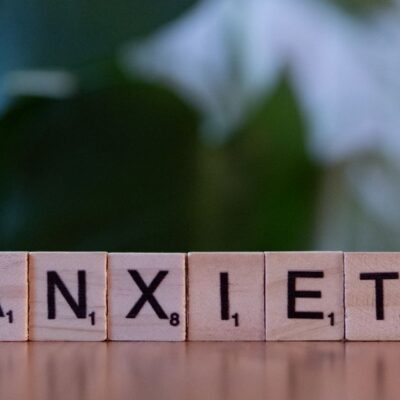Close-up of wooden blocks spelling ANXIETY on a wooden surface with blurred green background.
