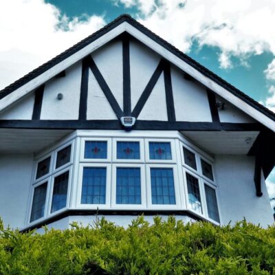 Tudor-style house facade with a bay window against a vibrant sky and greenery.