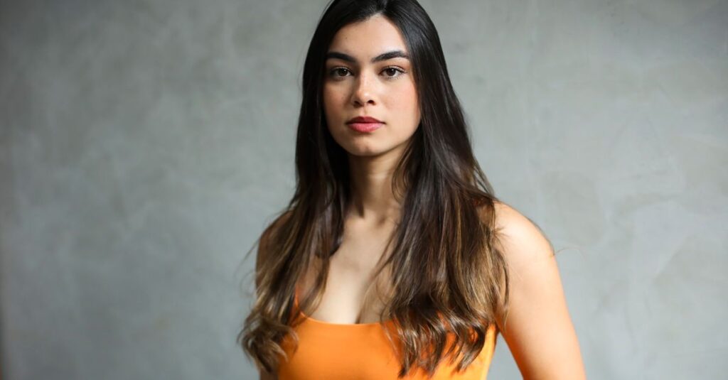 5 Dicas para Cultivar a Autoestima em Diferentes Fases da Vida 2 Elegant portrait of a young woman with long, dark hair in a vibrant orange top against a neutral background.