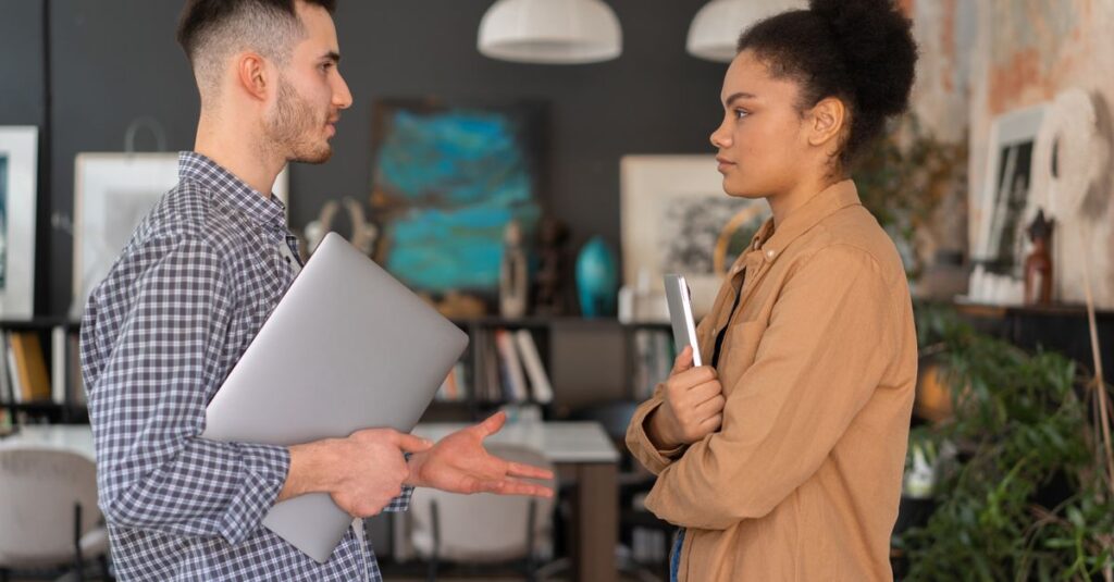 Two office workers engaged in a conversation, holding devices, in a modern office setting.