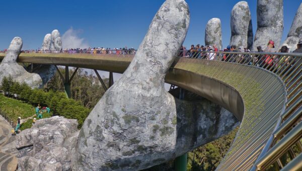 The iconic Golden Bridge with giant hand sculptures at Ba Na Hills, Vietnam, under a clear blue sky.