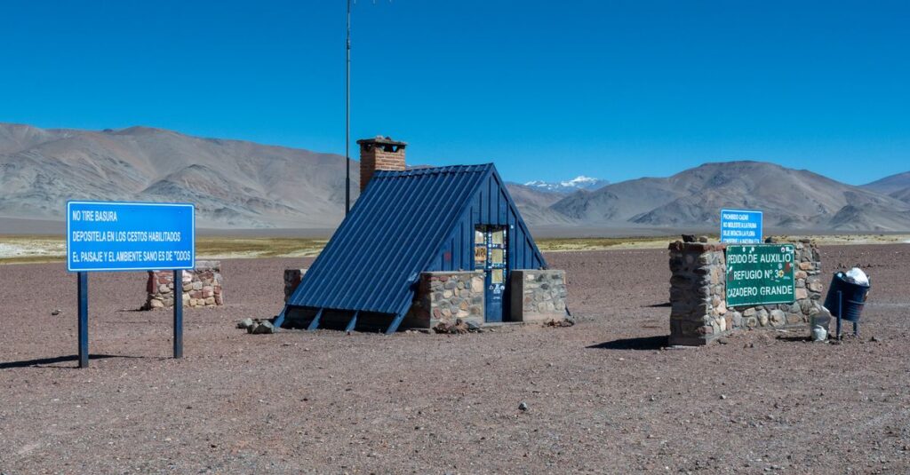 Stone shelter and signs against Andes Mountains in Catamarca, Argentina.