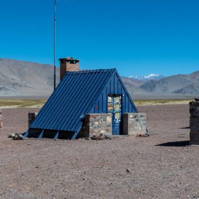Stone shelter and signs against Andes Mountains in Catamarca, Argentina.