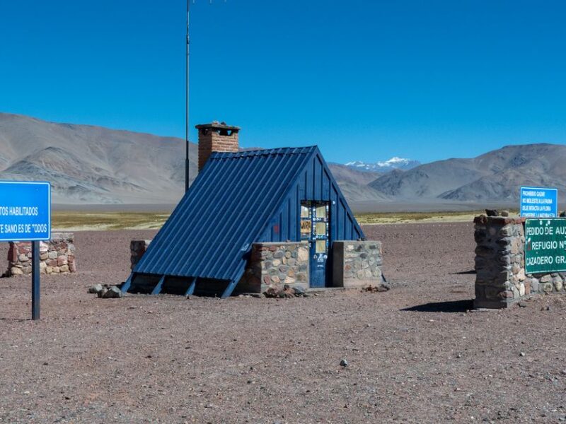 Stone shelter and signs against Andes Mountains in Catamarca, Argentina.