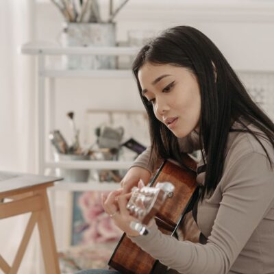 Asian woman taking an online guitar lesson at home using a laptop.