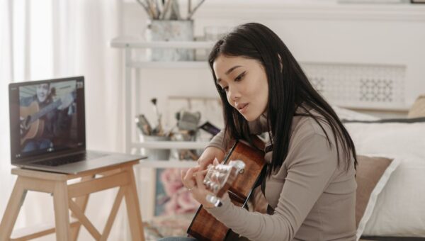 Asian woman taking an online guitar lesson at home using a laptop.