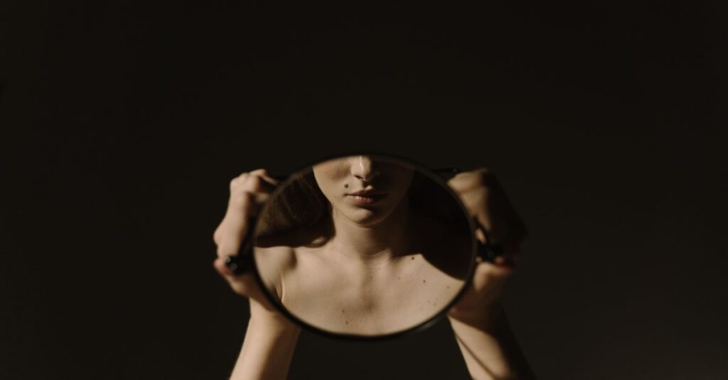 Artistic portrait of a woman holding a mirror, reflecting her face, with a dark, moody background.