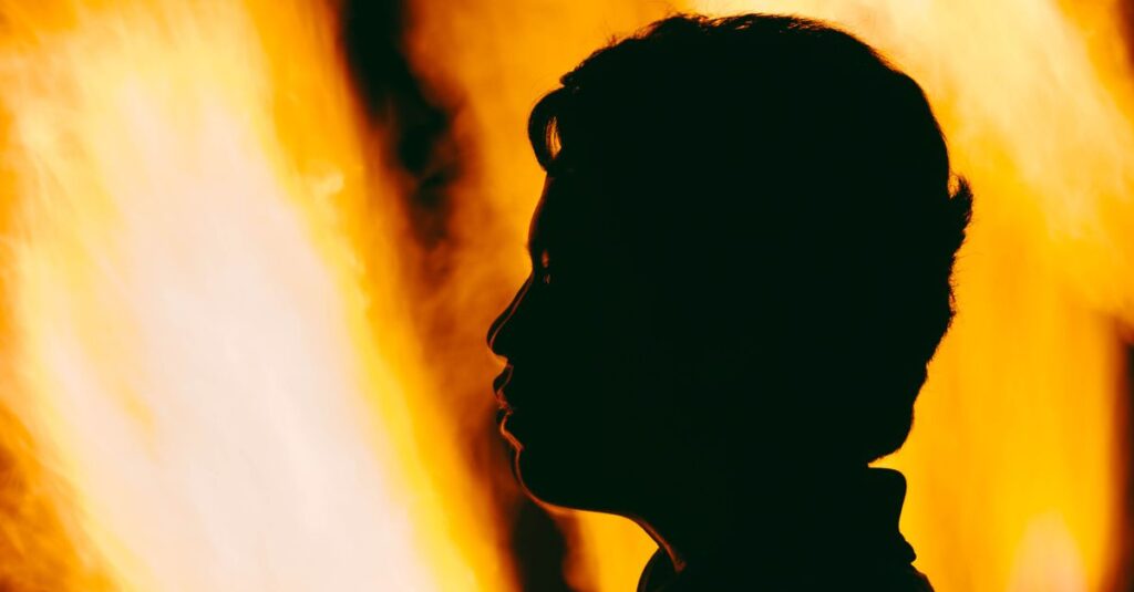 Como Cultivar a Resiliência Emocional no Dia a Dia 2 A dramatic silhouette of a person's profile against vivid orange flames.