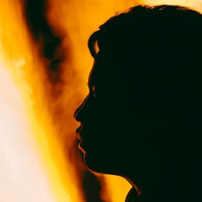 A dramatic silhouette of a person's profile against vivid orange flames.
