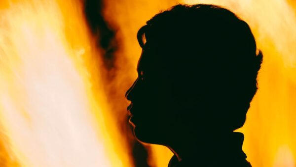 A dramatic silhouette of a person's profile against vivid orange flames.